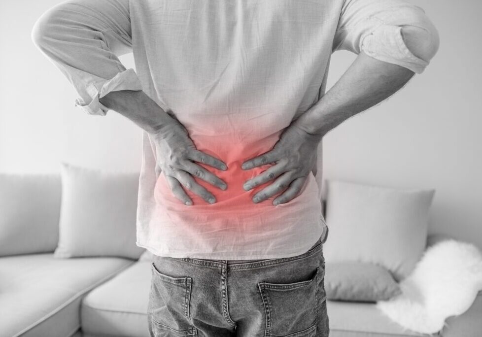 Close up of a man holding his back in pain, monochrome photo with red as a symbol for the hardening. Man suffering from back ache on gray background. Health care concept
